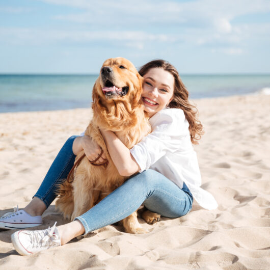 Happy woman sitting and hugging her dog on the beach